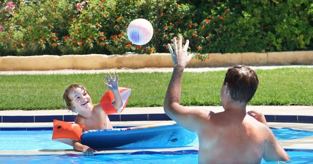 Pai segurando bola colorida na piscina para incentivar a criança com TEA a interagir.