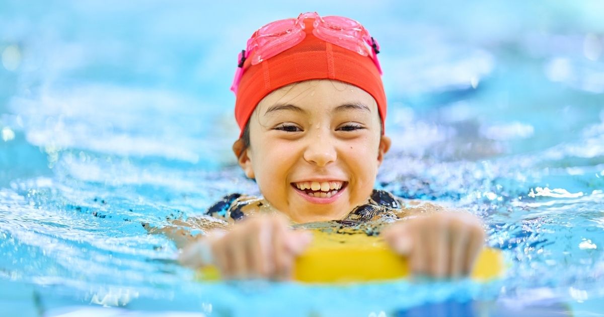 Criança com TEA sorrindo na piscina enquanto segura brinquedo flutuante.