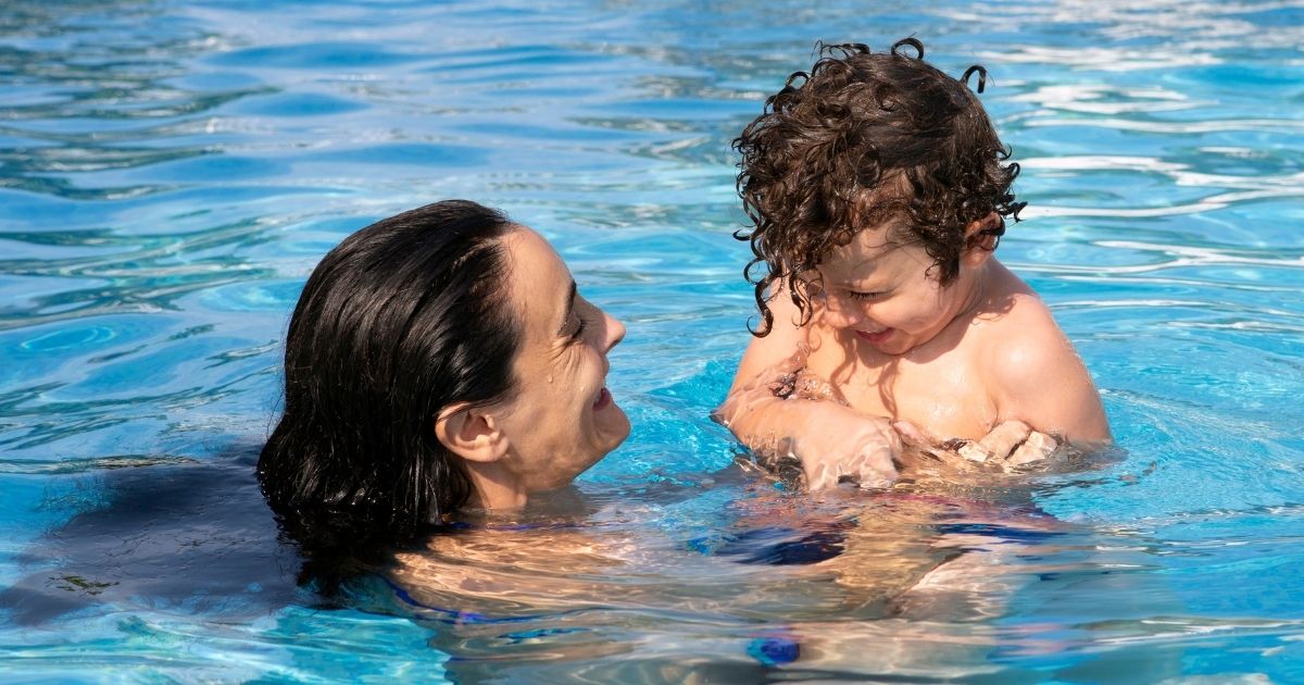 Mãe ajudando filho autista a se adaptar na água com brinquedos sensoriais